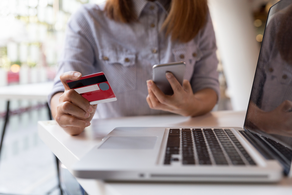 Woman holding credit card and smartphone while shopping online on laptop.