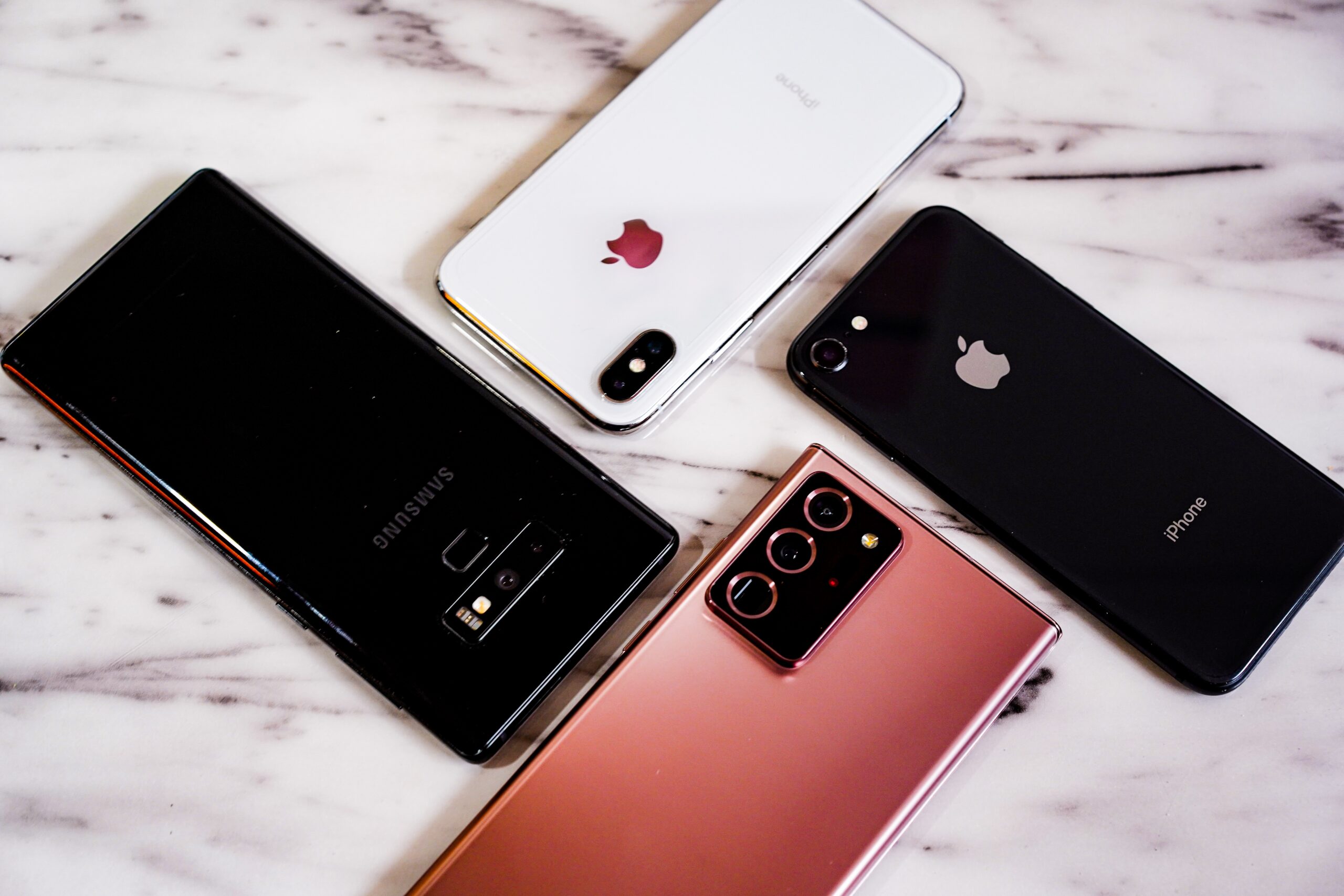 Apple iPhone and Samsung Galaxy smartphones arranged on a marble surface showing rear camera designs.