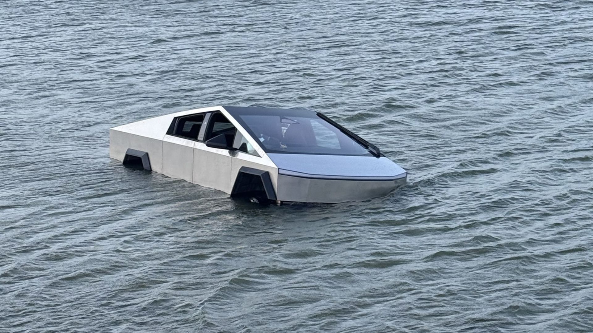 Tesla Cybertruck partially submerged in a lake with only the upper half of the vehicle visible above the water.