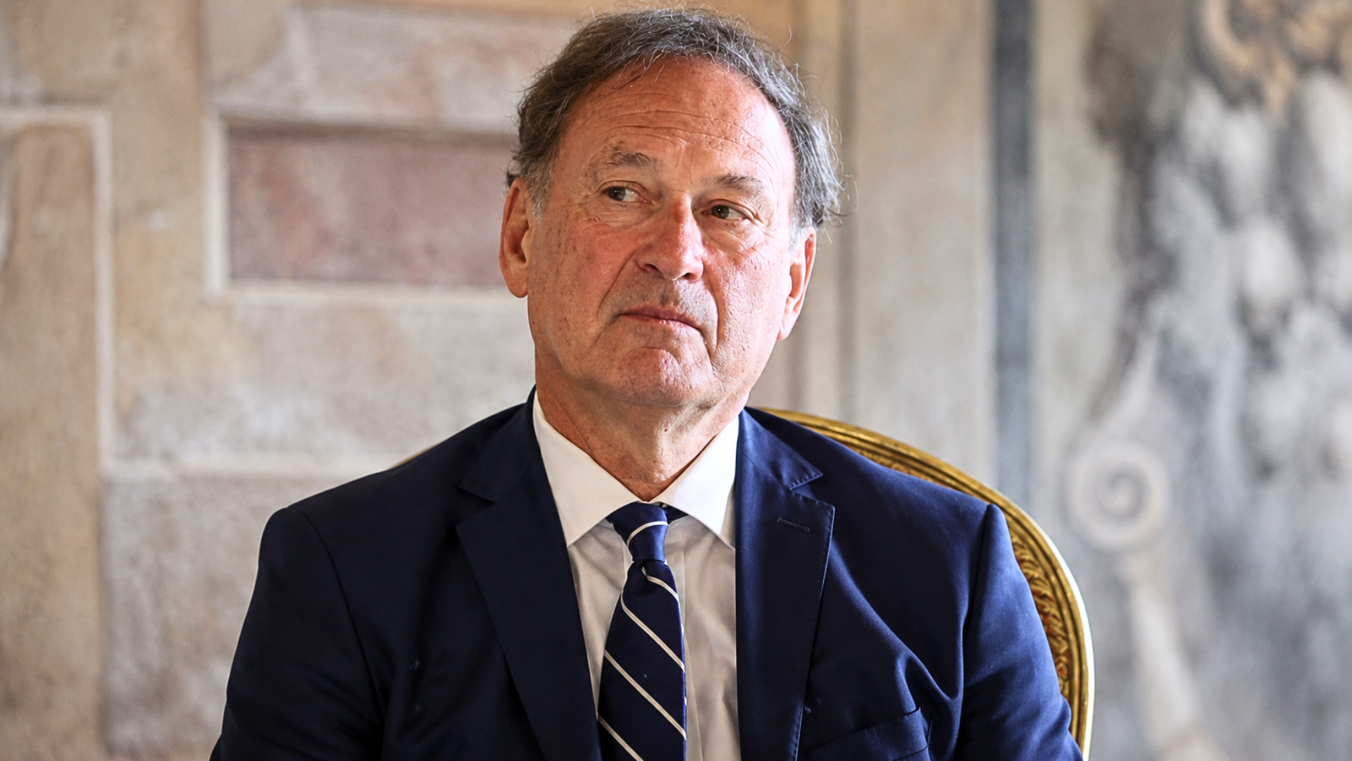A close-up, slightly low-angle portrait of Justice Samuel Alito looking thoughtfully toward the side.