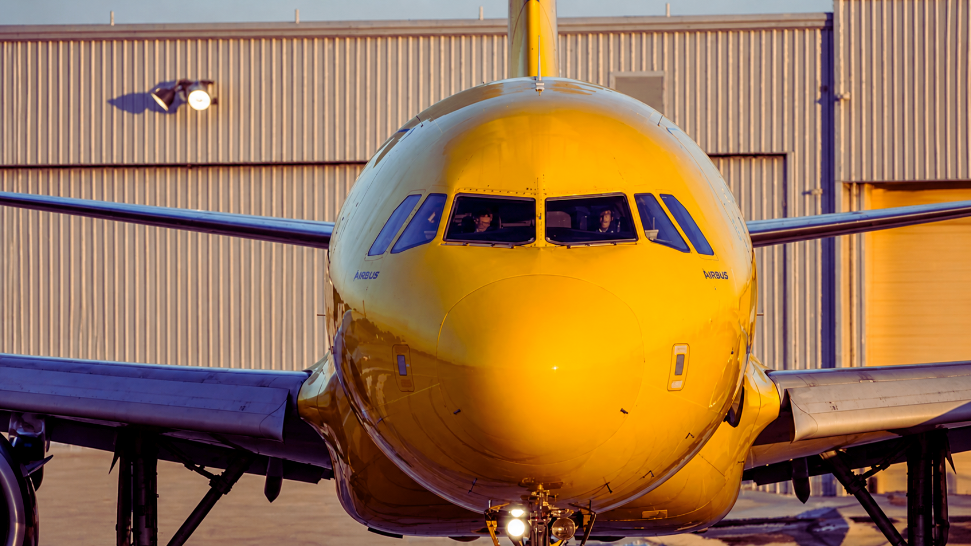 A close-up, head-on view of the nose and cockpit of a bright yellow Spirit Airlines Airbus jet.