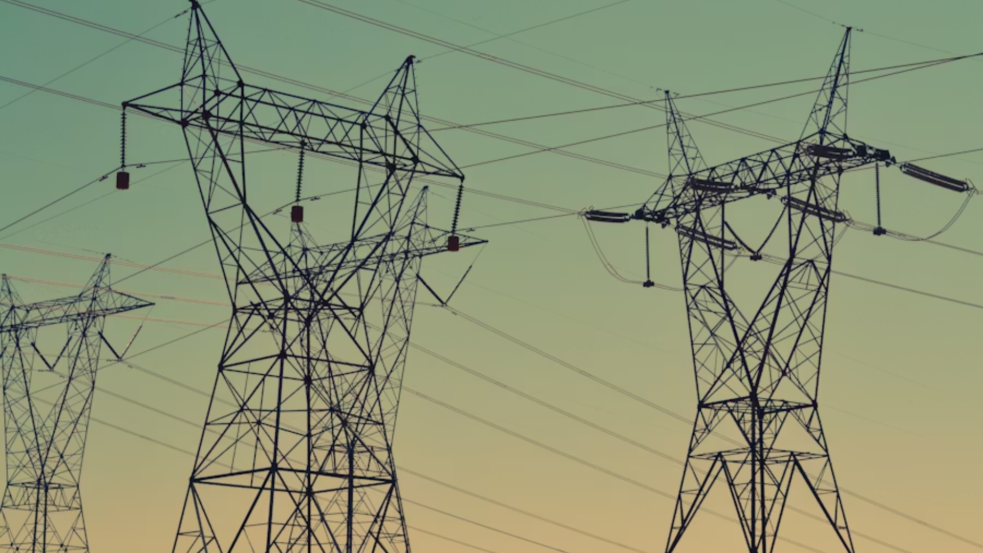 A low-angle shot at dusk showing three massive steel lattice high-voltage power transmission towers holding up interlocking arrays of electrical cables against a smooth, gradient sky transitioning from teal to soft orange.