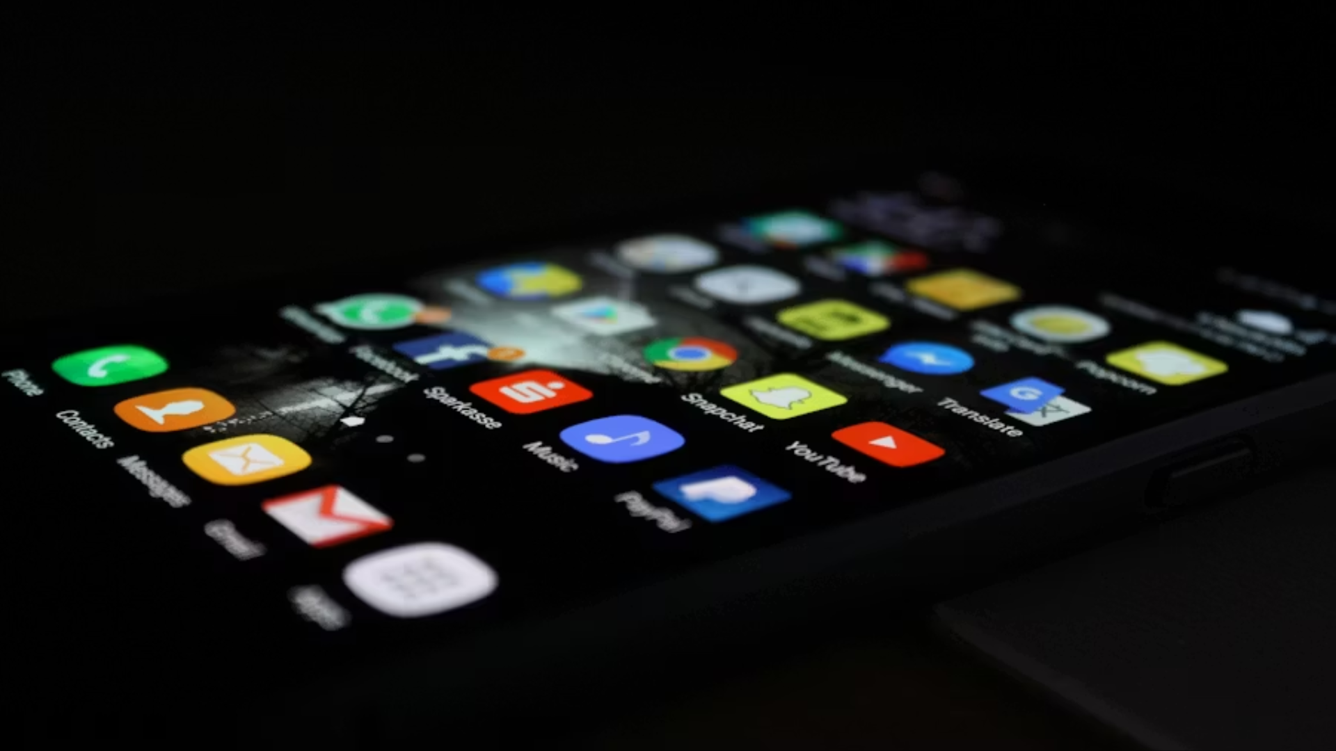 A close-up, low-angle view of a smartphone screen illuminated in the dark, displaying a grid of colorful mobile application icons.