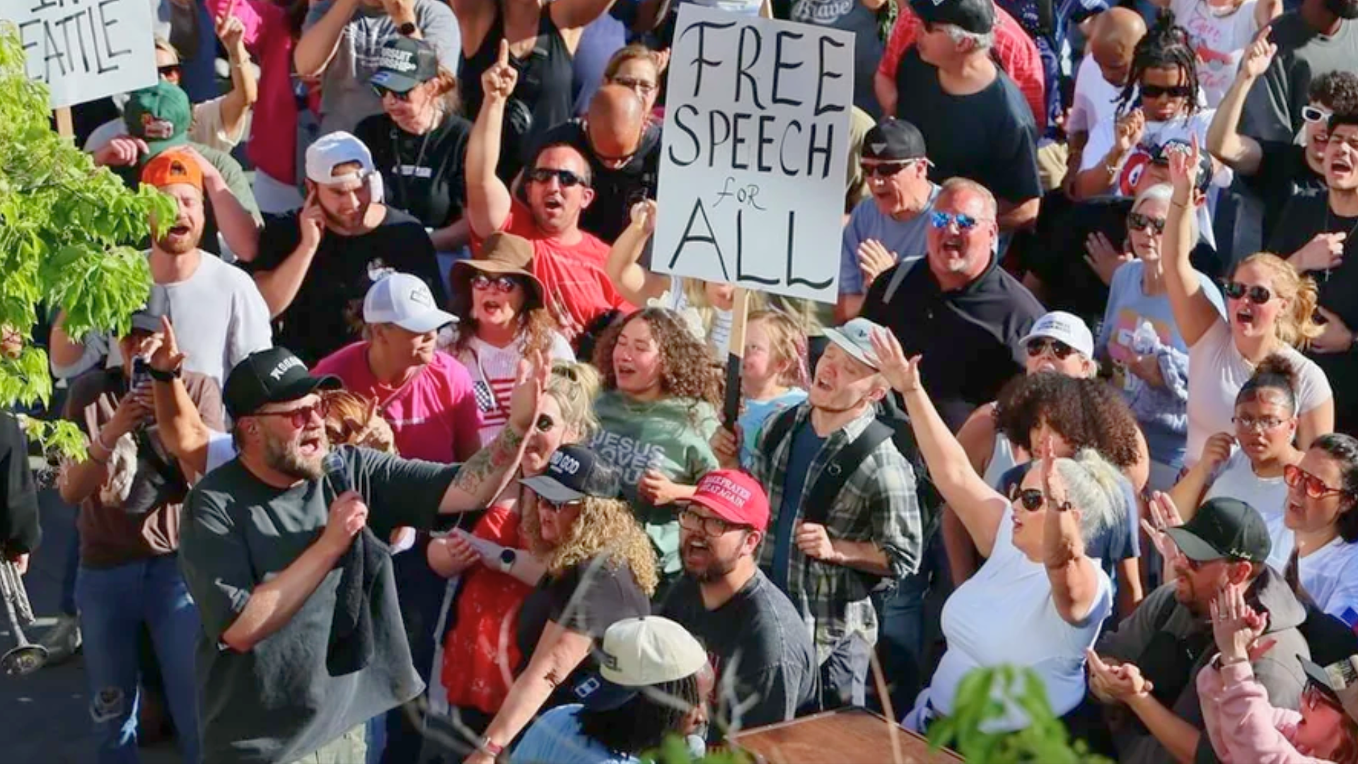 Crowd of protesters holding a “Free Speech for All” sign during a rally.