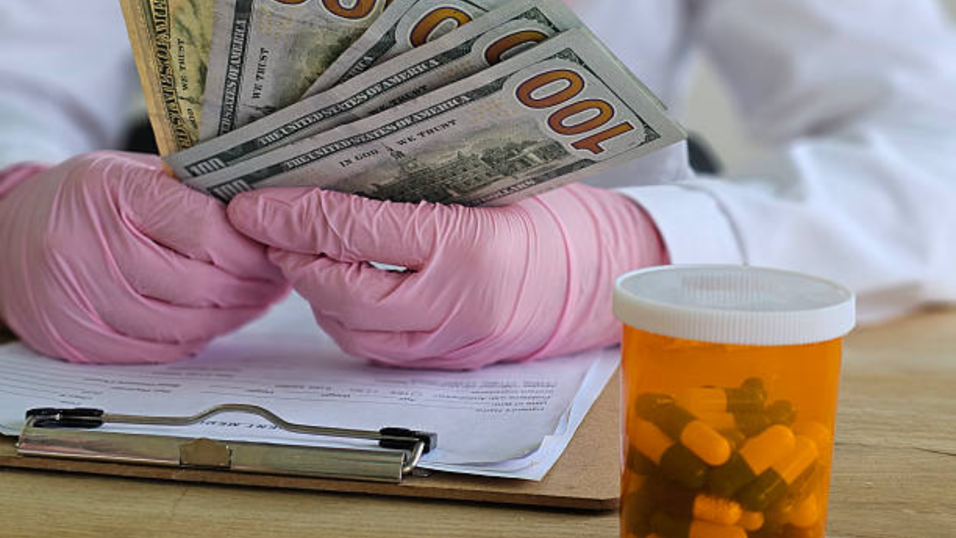 Medical worker holding cash beside a prescription bottle filled with pills.