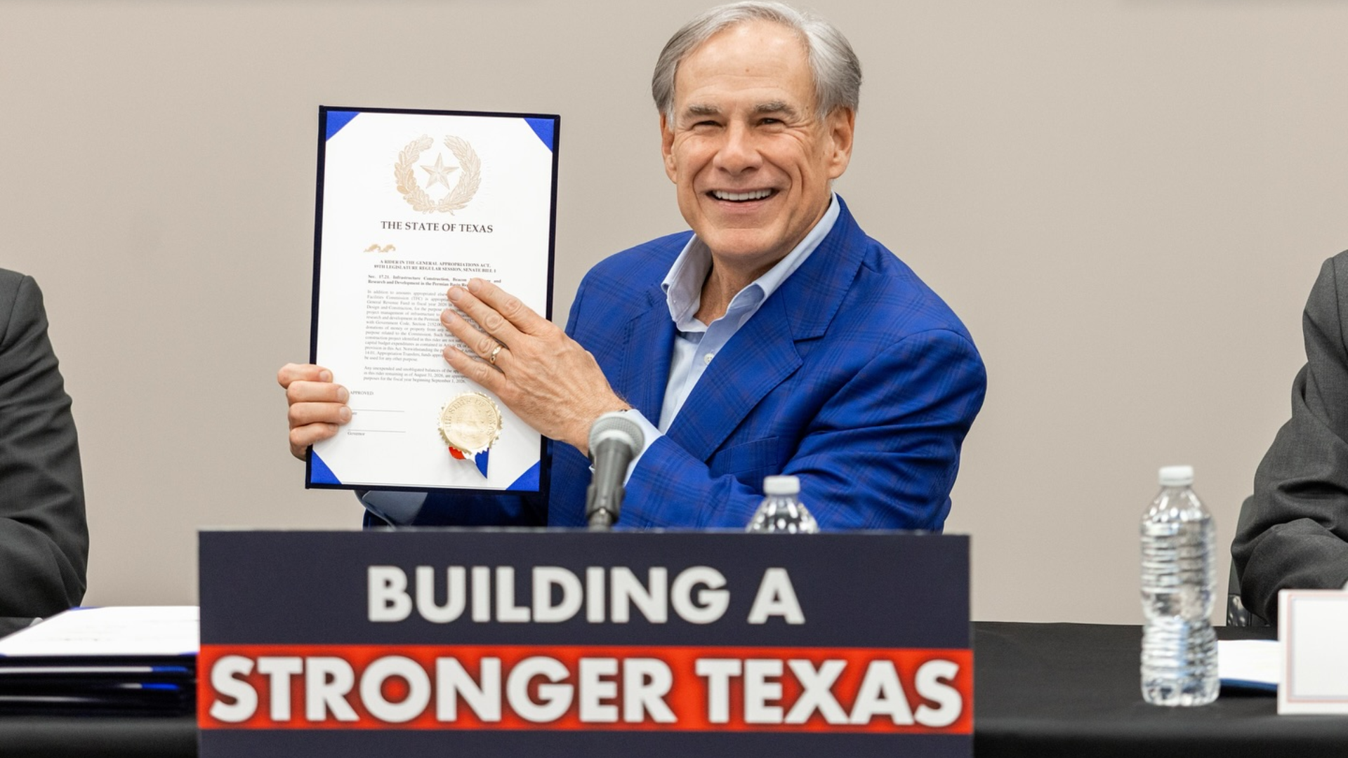 A medium shot of Texas Governor Greg Abbott smiling broadly at a press conference.