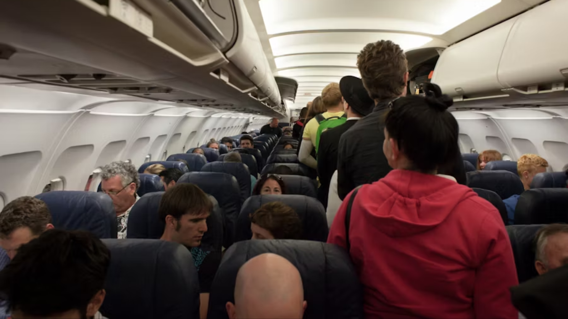 A shot from the back of a crowded airplane cabin looking toward the front.