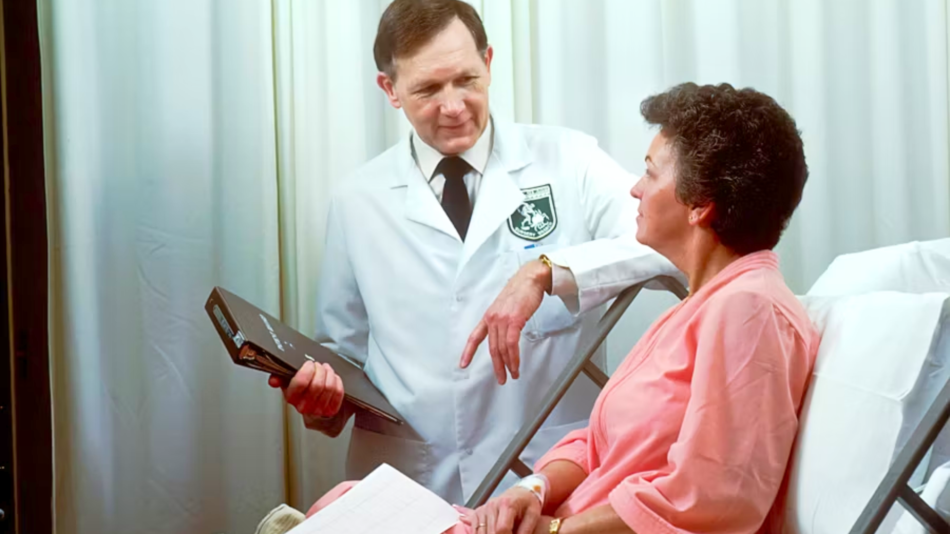 Doctor speaking with a patient seated in a hospital examination room.