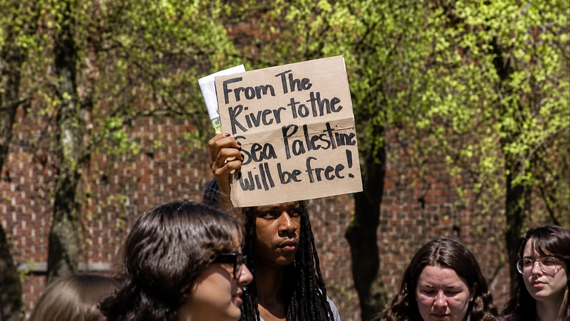 Protester holding sign reading “From the river to the sea Palestine will be free” at a demonstration.