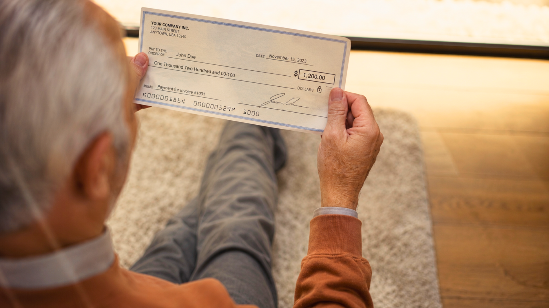 An over-the-shoulder, high-angle shot of an older man holding a paper business check.
