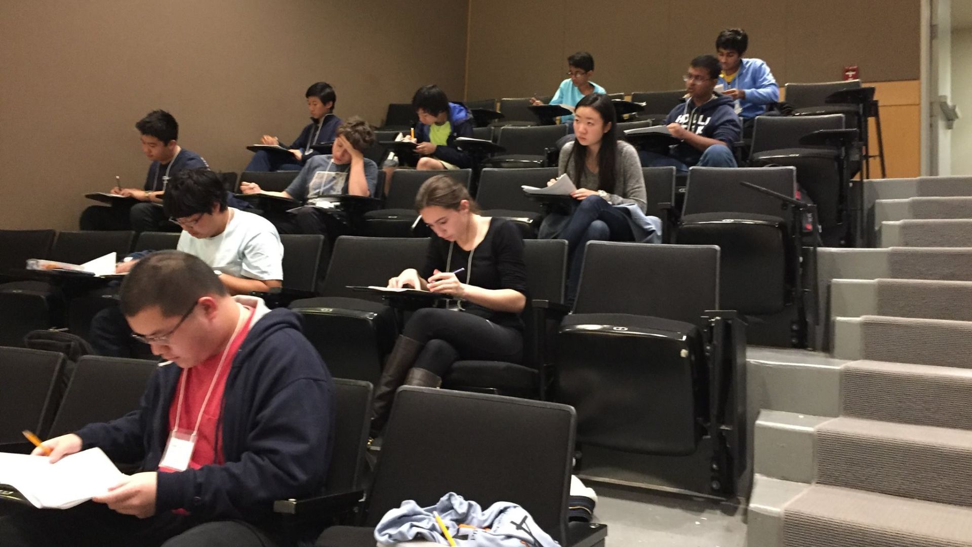 Students sit throughout a tiered lecture hall while taking notes and completing coursework during class.