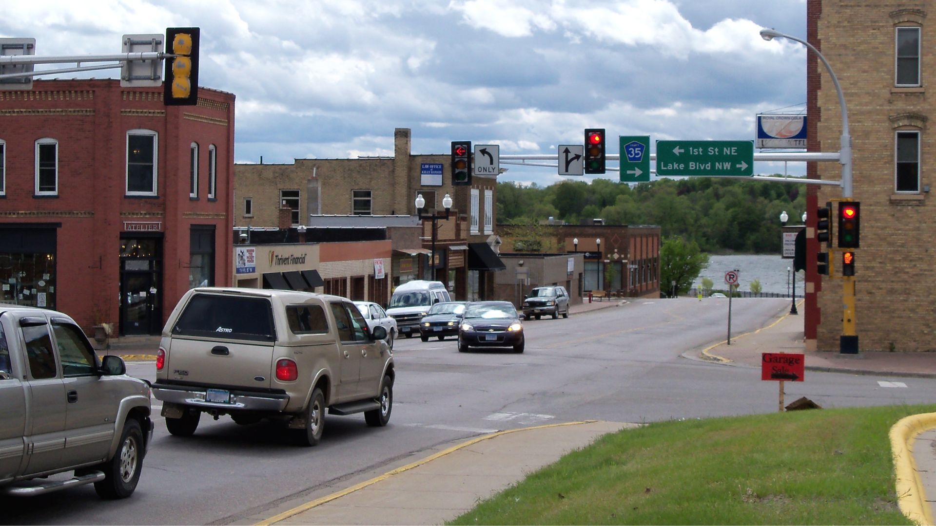 Small town intersection with traffic lights and street signs including "1st St NE" and "Lake Blvd NW" as cars drive through.