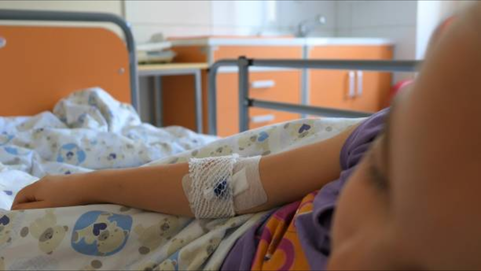 Child resting in a hospital bed with an IV bandage on their arm.
