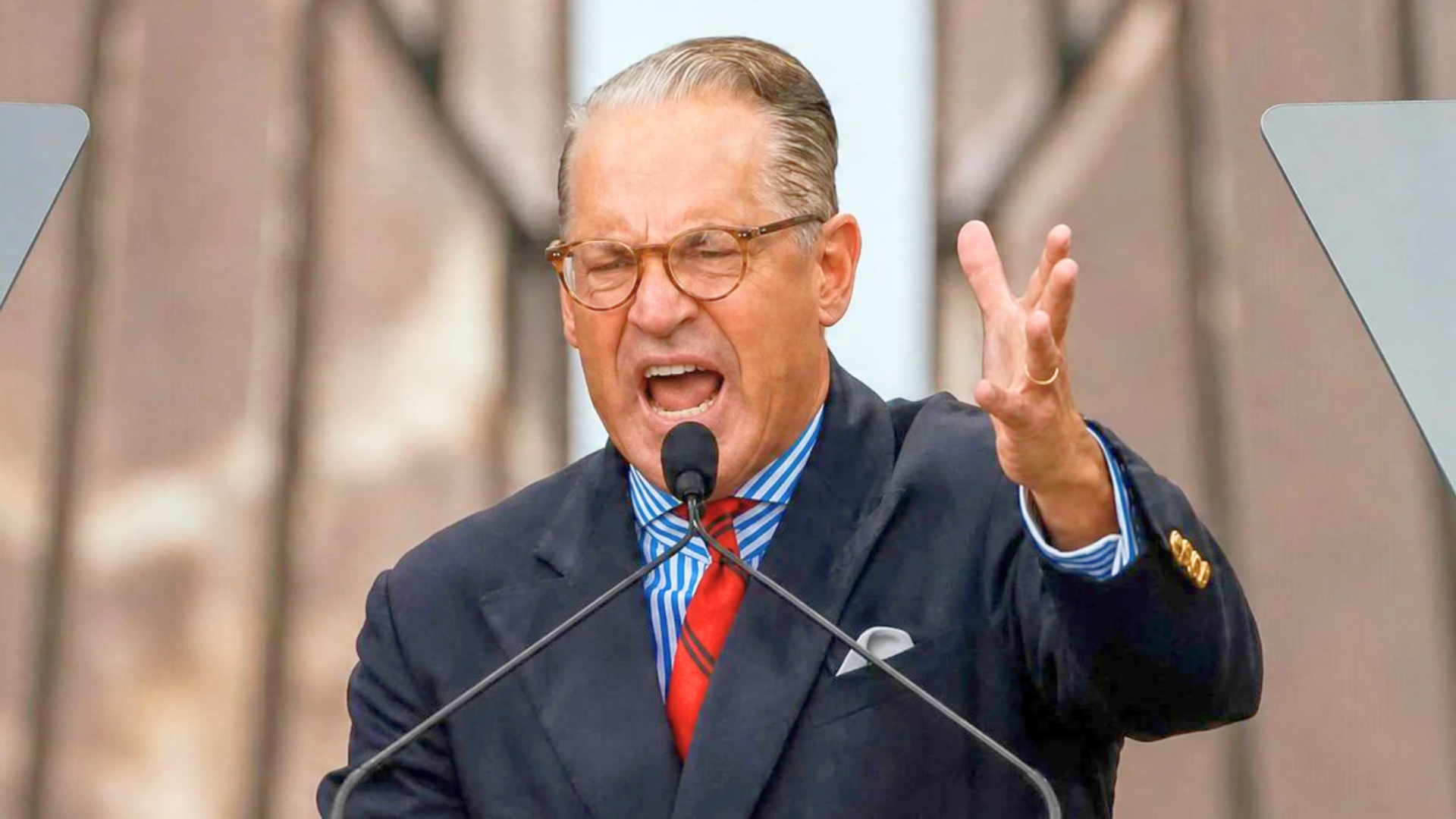 Eric Metaxas speaks passionately into a microphone at a podium with his hand raised.