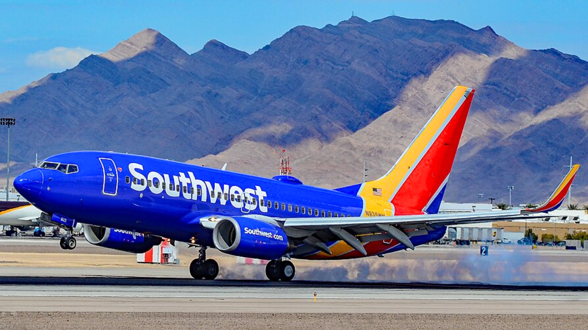 A bright blue Southwest Airlines plane on an airport runway with large brown mountains in the background.