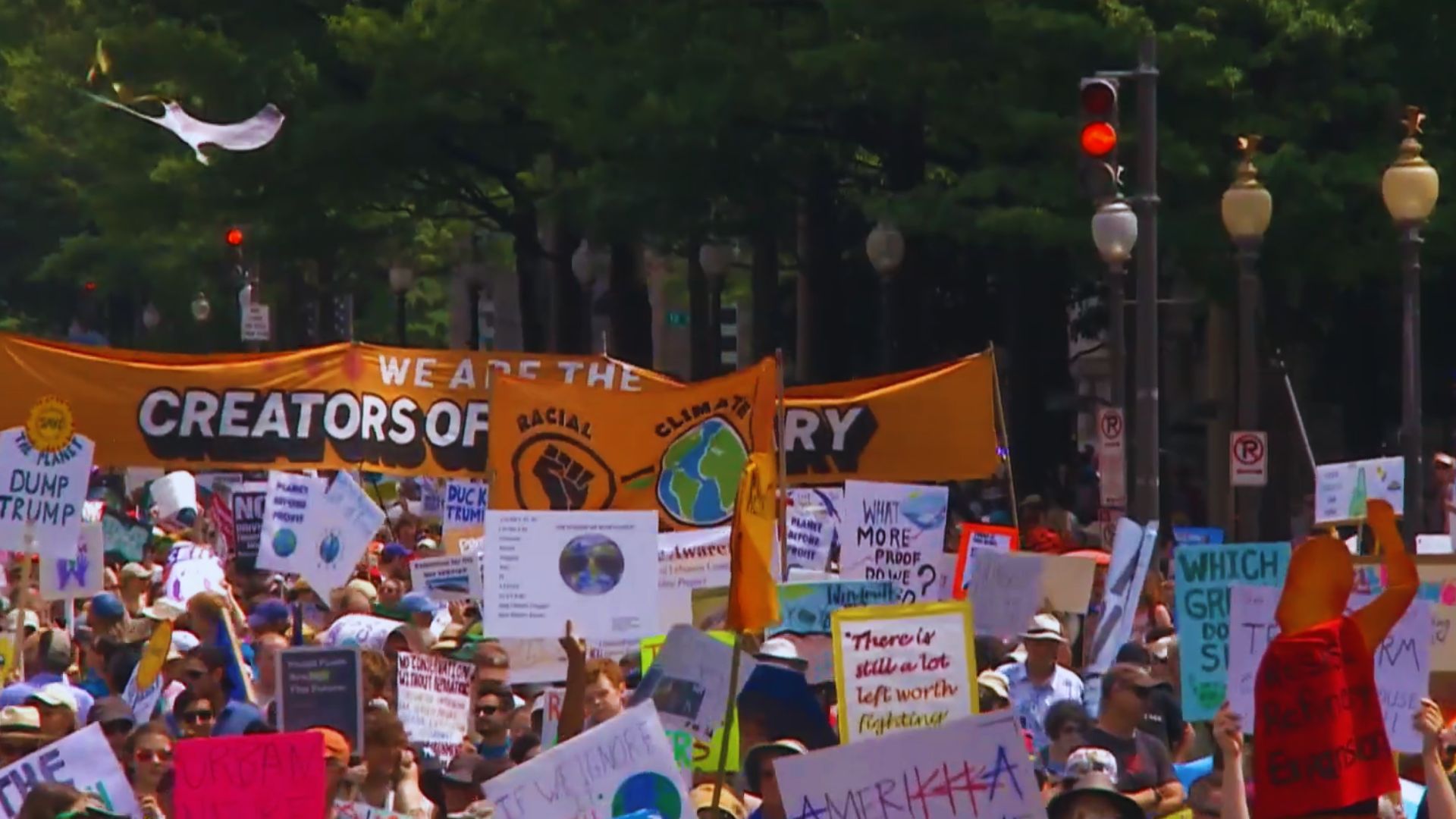 Large crowd of climate activists and environmental protesters march through a city street carrying banners and sign.