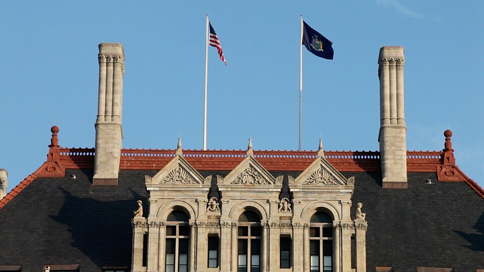 The US and NYS flags fly over the state capitol building in Albany, New York.