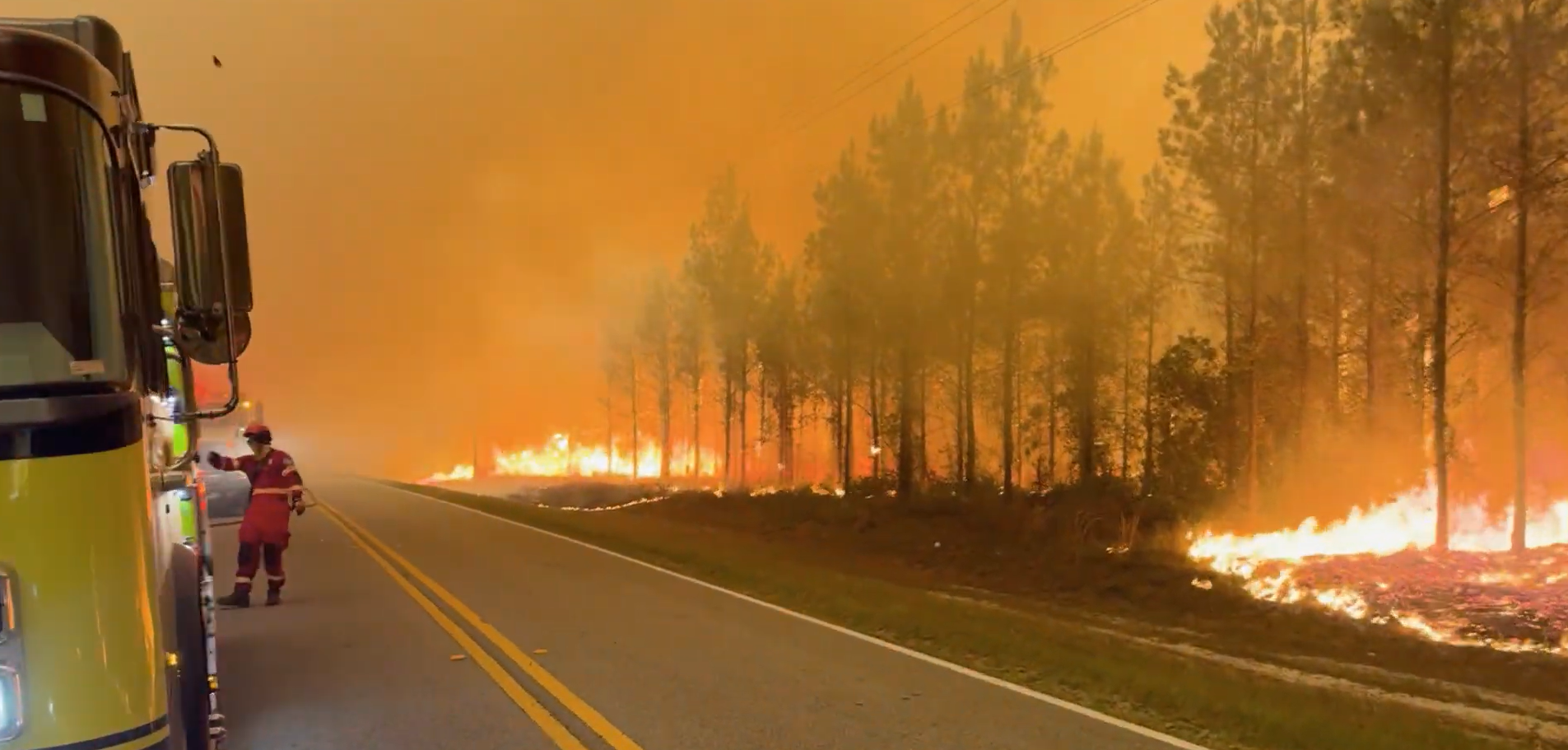 Firefighter standing near truck during an on scene response as wildfire burns along roadside in Brantley County, Georgia.