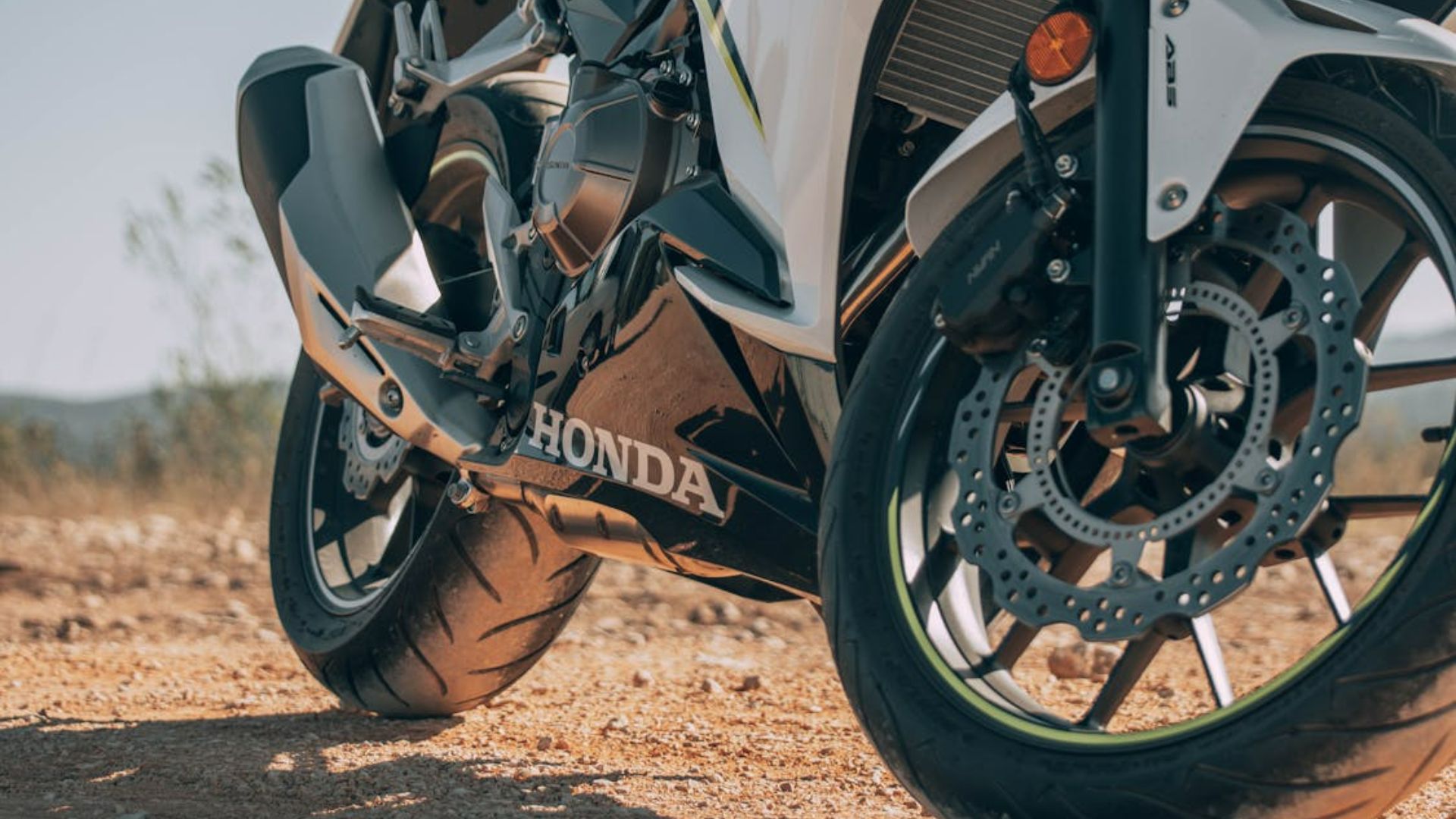 Close-up of a Honda motorcycle parked on a gravel road showing the engine and front wheel.