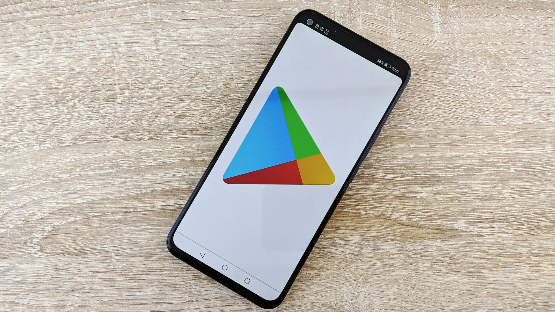 A smartphone rests diagonally on a light-colored wooden surface, displaying the multicolored Google Play Store logo on its screen.