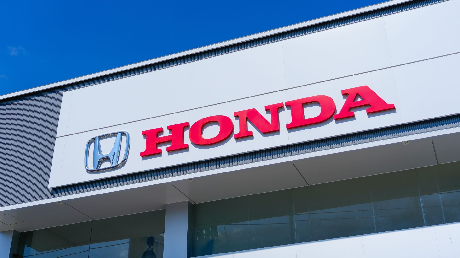 Honda logo and emblem on the facade of a white commercial building against a clear blue sky.