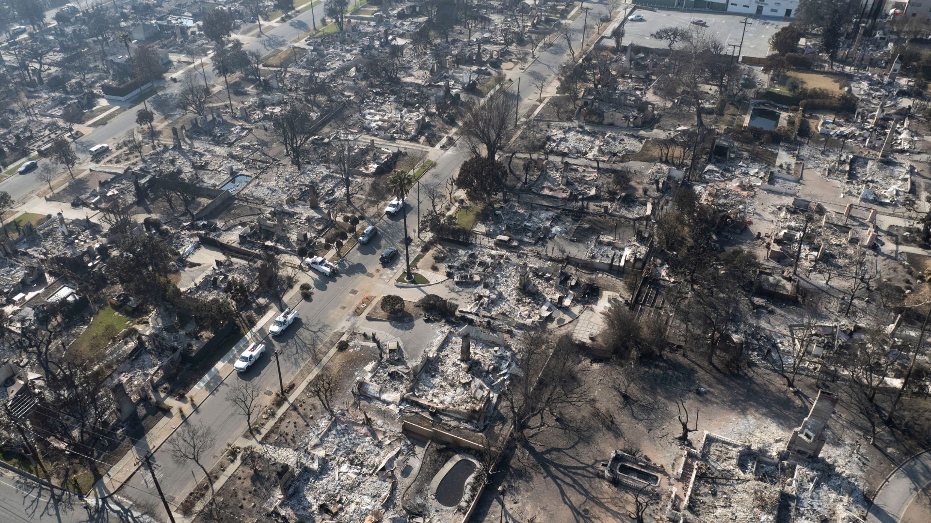 Aerial view of a residential neighborhood completely devastated by wildfire, with homes reduced to ash and rubble.
