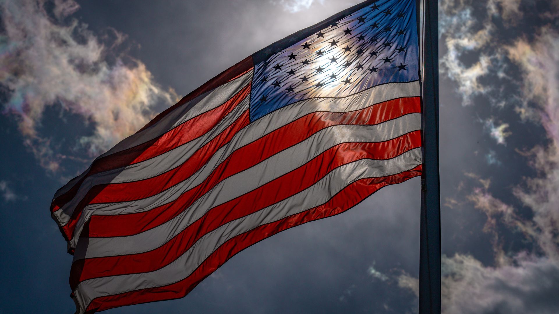 American flag waving on a pole against a cloudy sky.