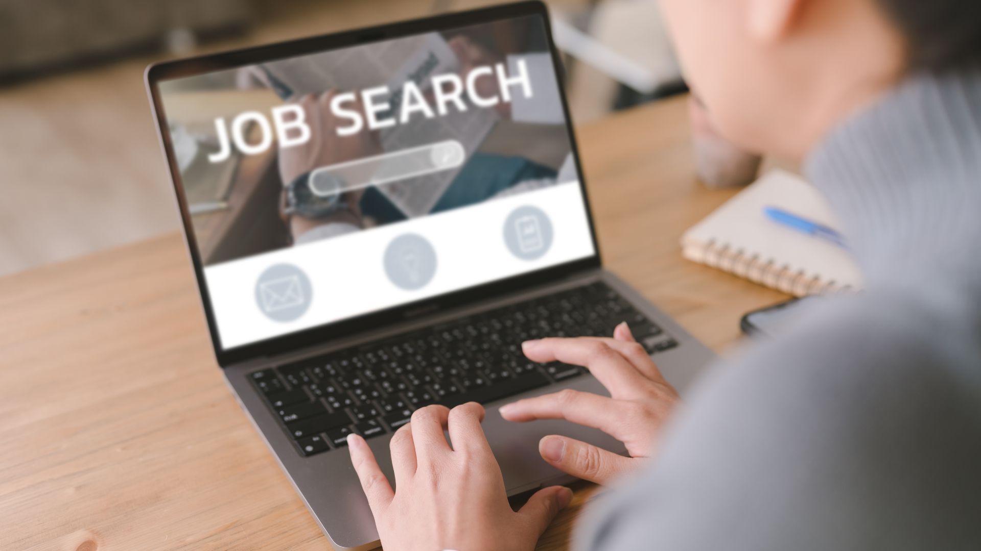 Person searching for jobs on a laptop at a wooden desk.