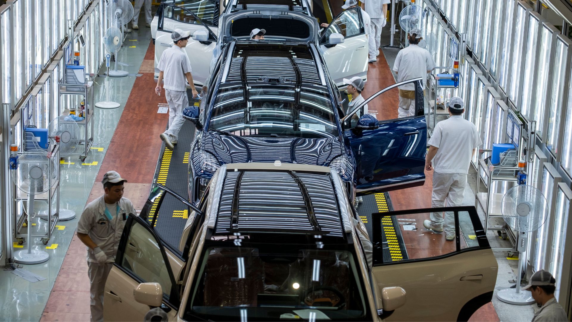 Workers inspecting vehicles along an electric car production assembly final inspection line.