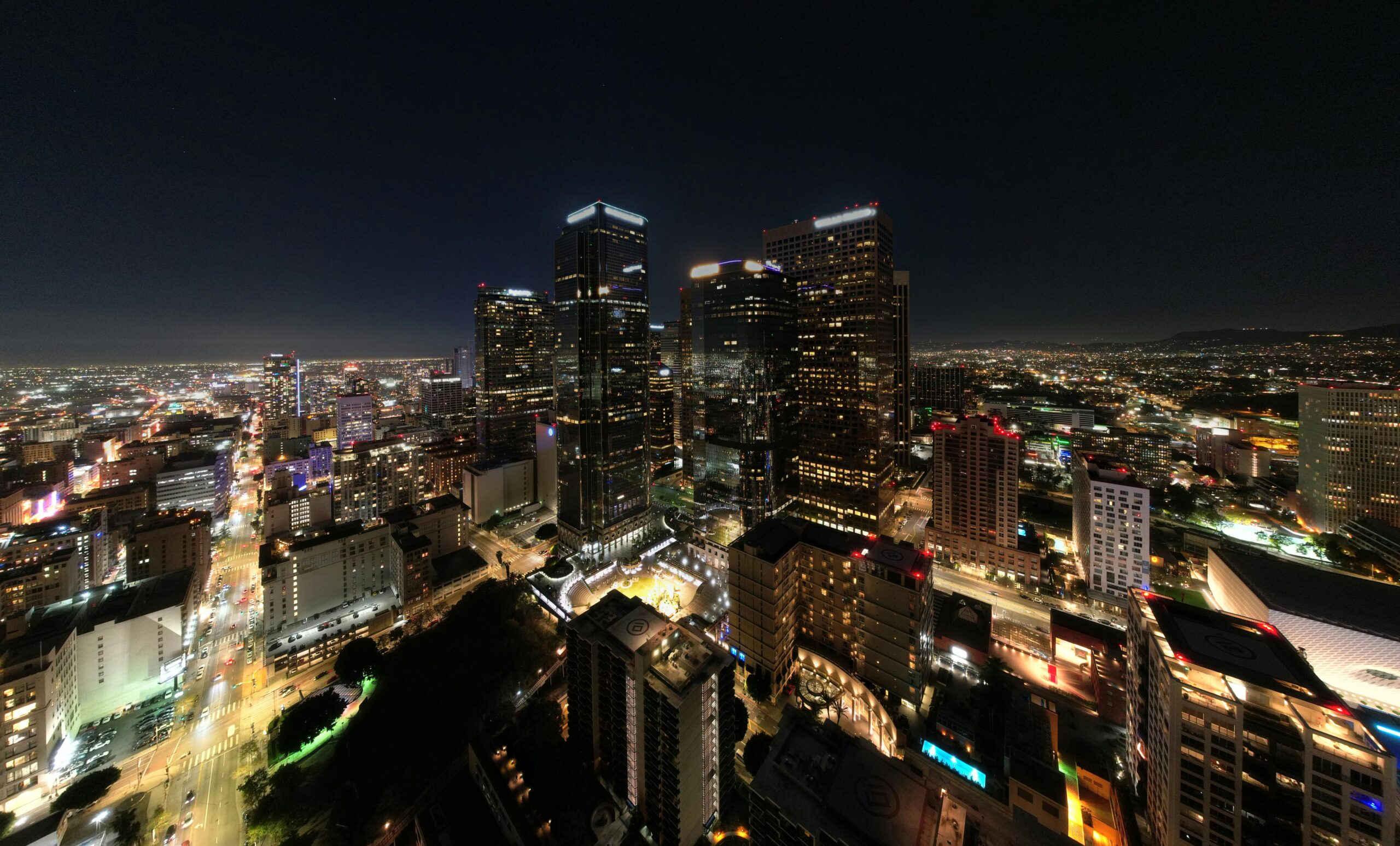 Nighttime aerial view of downtown Los Angeles skyline with illuminated skyscrapers and city streets.