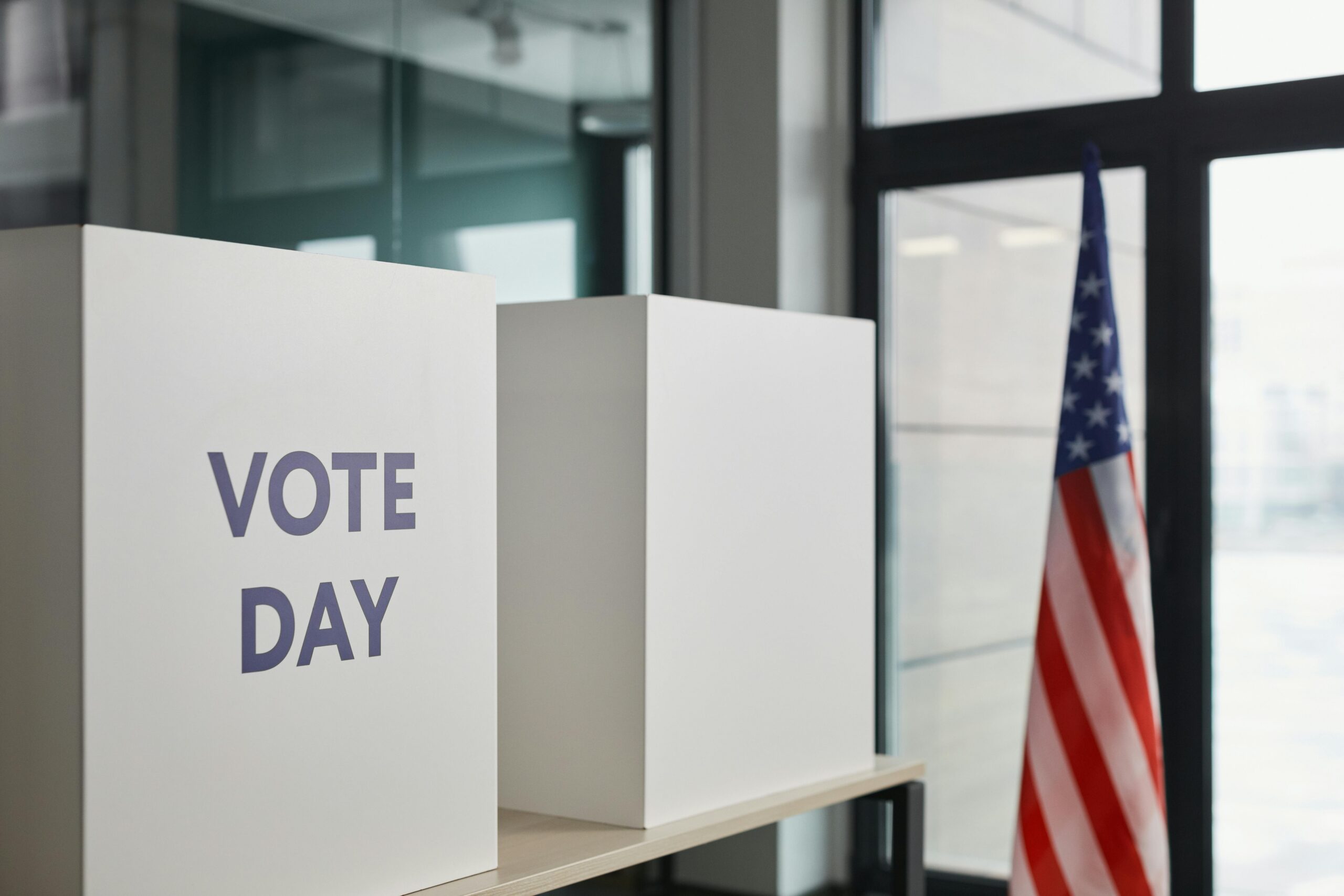 Voting booths labeled “Vote Day” beside an American flag inside a polling location.