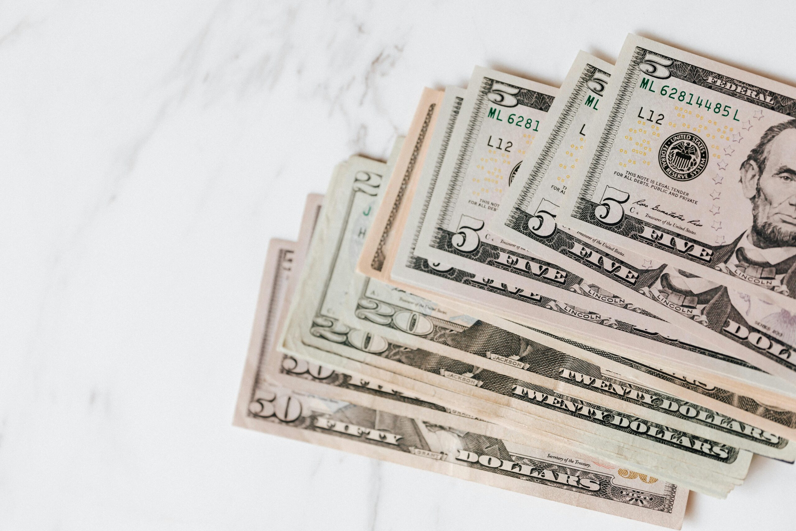 Stack of U.S. dollar bills including $5, $20, and $50 notes arranged on a white surface.