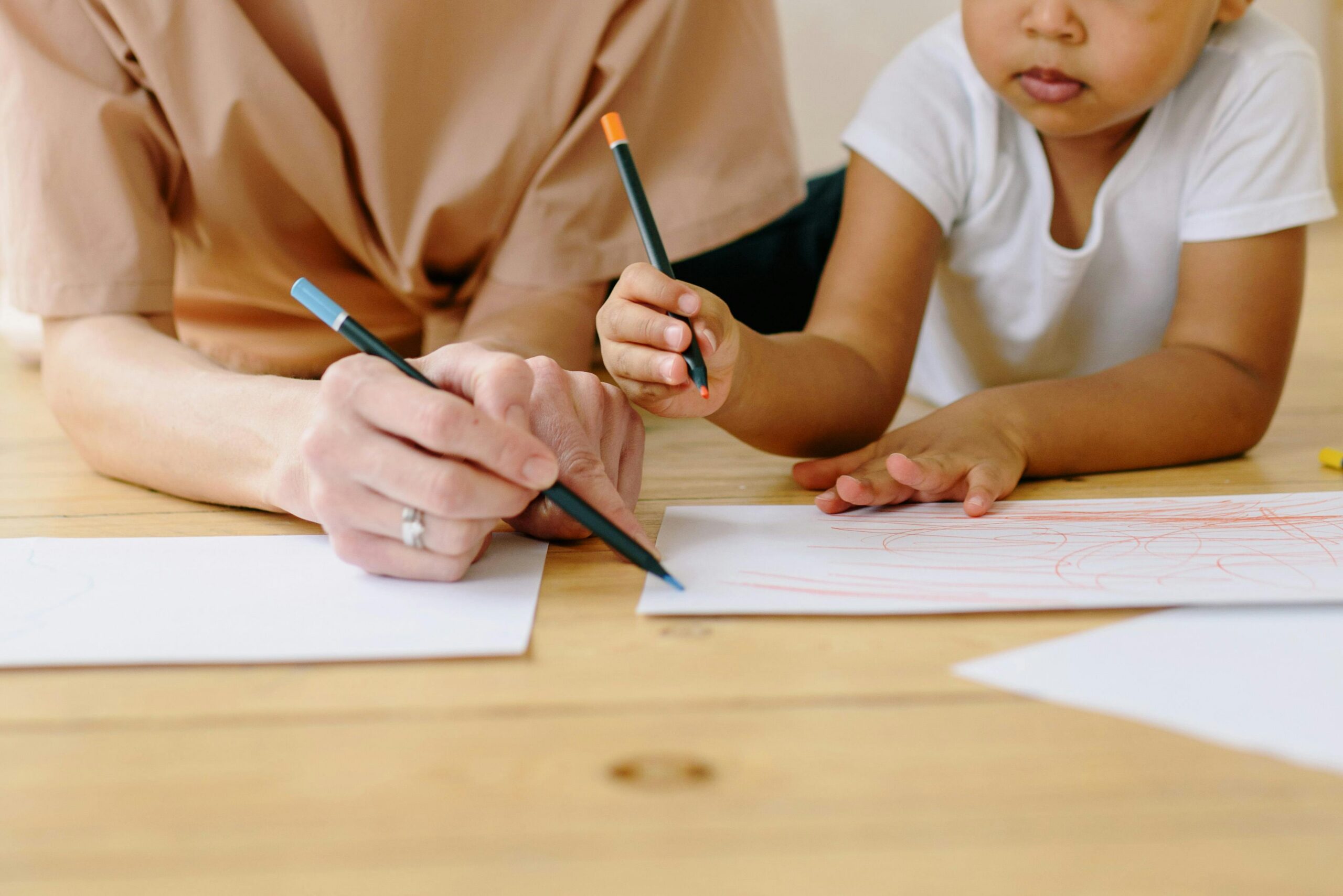 A young child and adult sit at a table drawing together during an autism therapy or developmental support session.