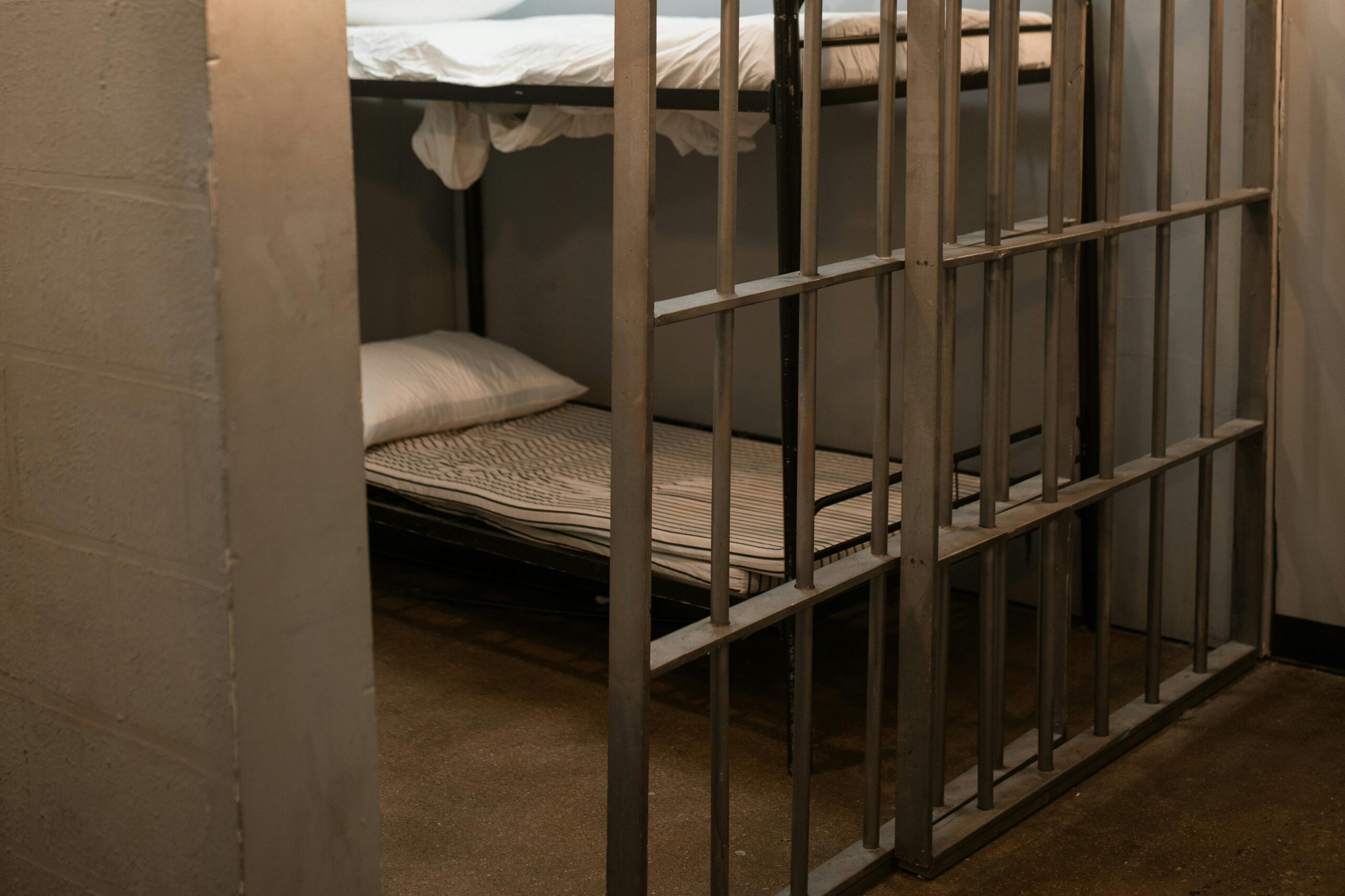 Empty jail cell with metal bars and bunk beds inside a detention facility.