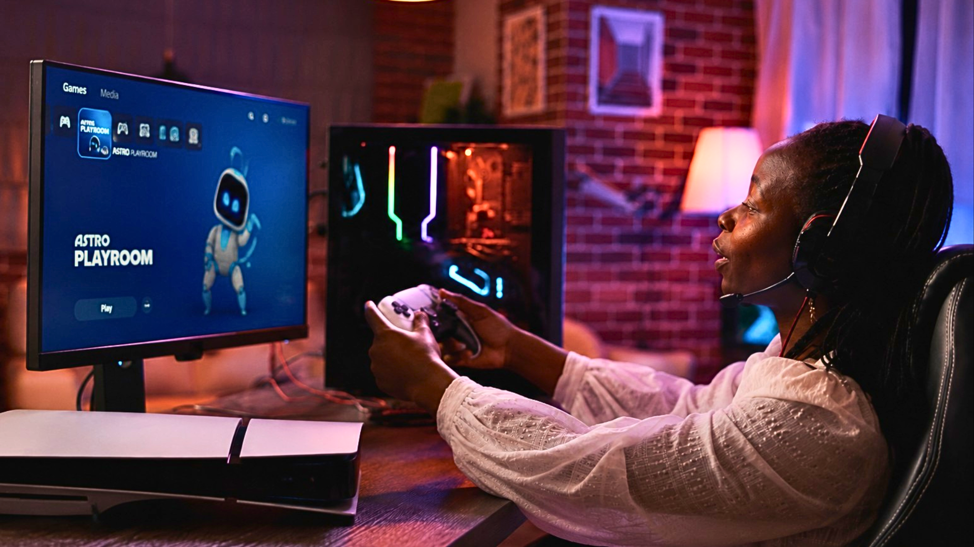 A medium shot of a young woman with braided hair wearing a white blouse and a gaming headset, holding a DualSense Edge controller while playing Astro Bot on a large monitor; a white PS5 Slim console is visible on the desk in the foreground in a room lit with red and blue LED lights.