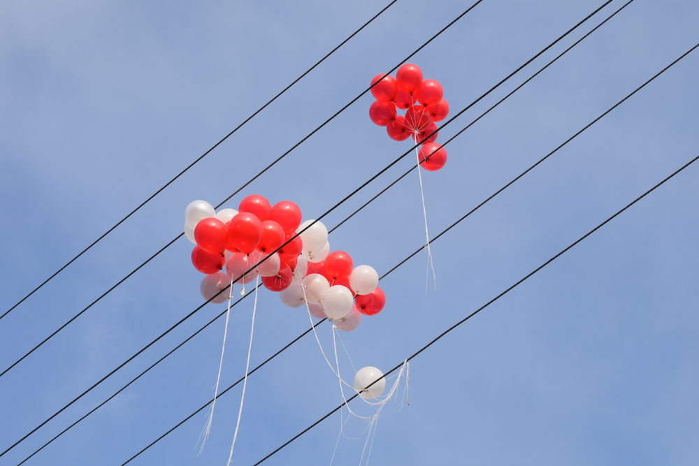 Red and white balloons tangled in overhead power lines against a clear sky.