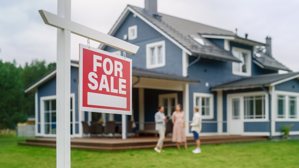 A family visiting a house for sale and a sign in the front part of the image.