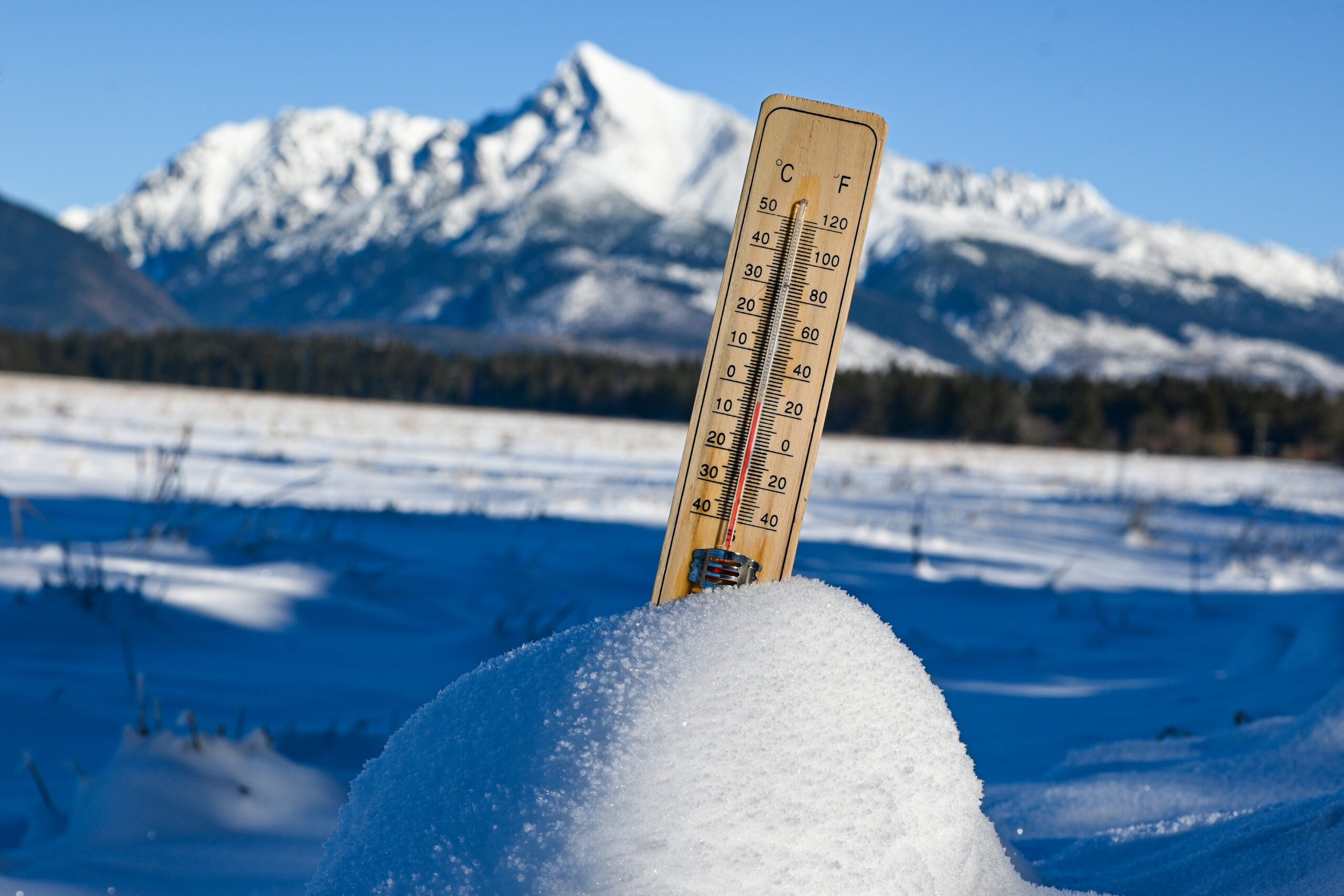 Thermometer standing in deep snow with snow-covered mountains in the background.