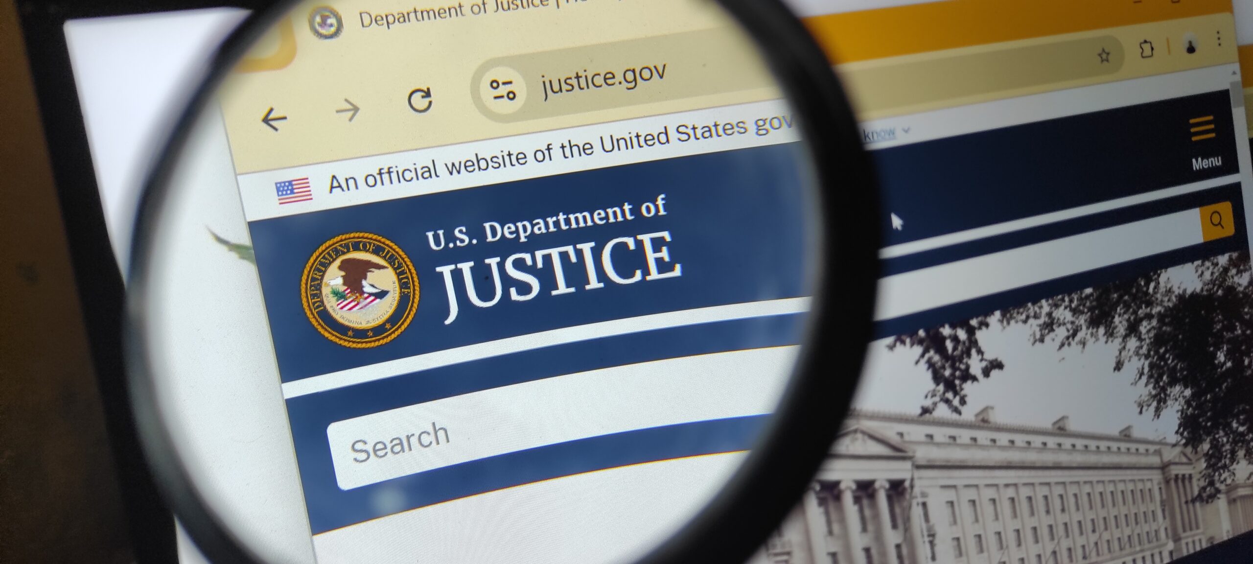 A magnifying glass hovers over the U.S. Department of Justice website displayed on a computer screen during a federal fraud investigation concept image.