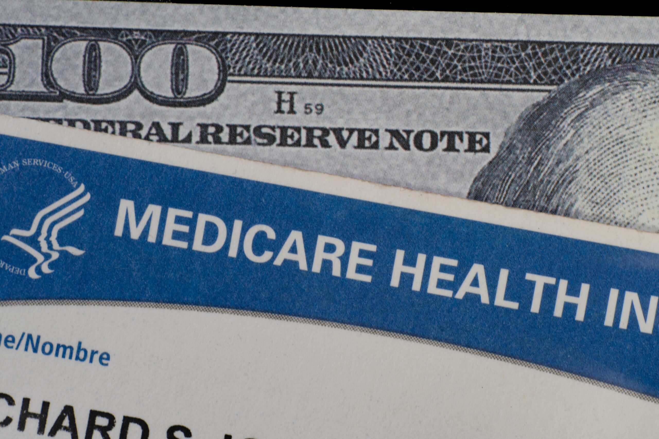 Close-up of a Medicare health insurance card placed beside a U.S. $100 bill.