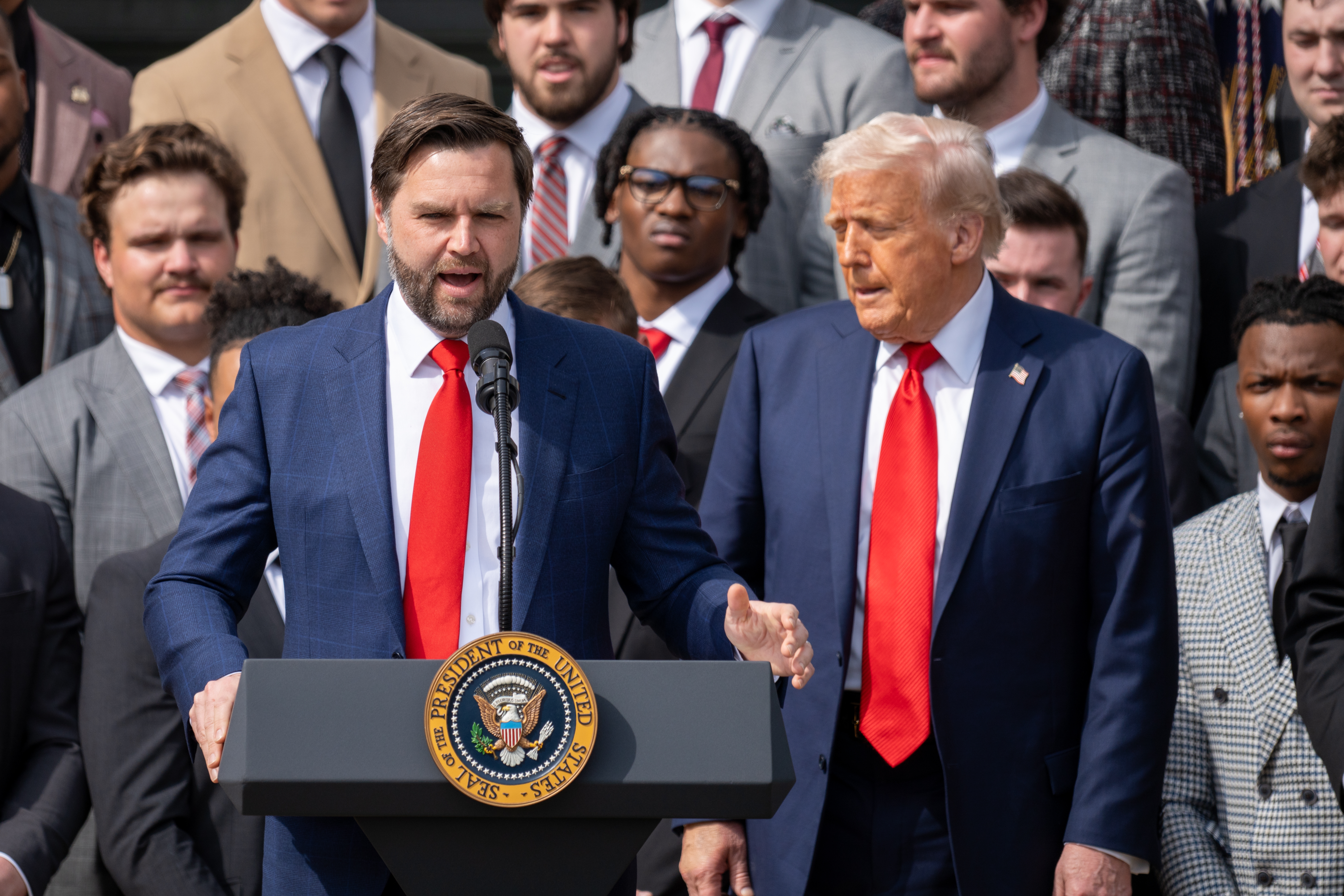 Vice President-elect JD Vance speaking at a podium beside Donald Trump during a public event.