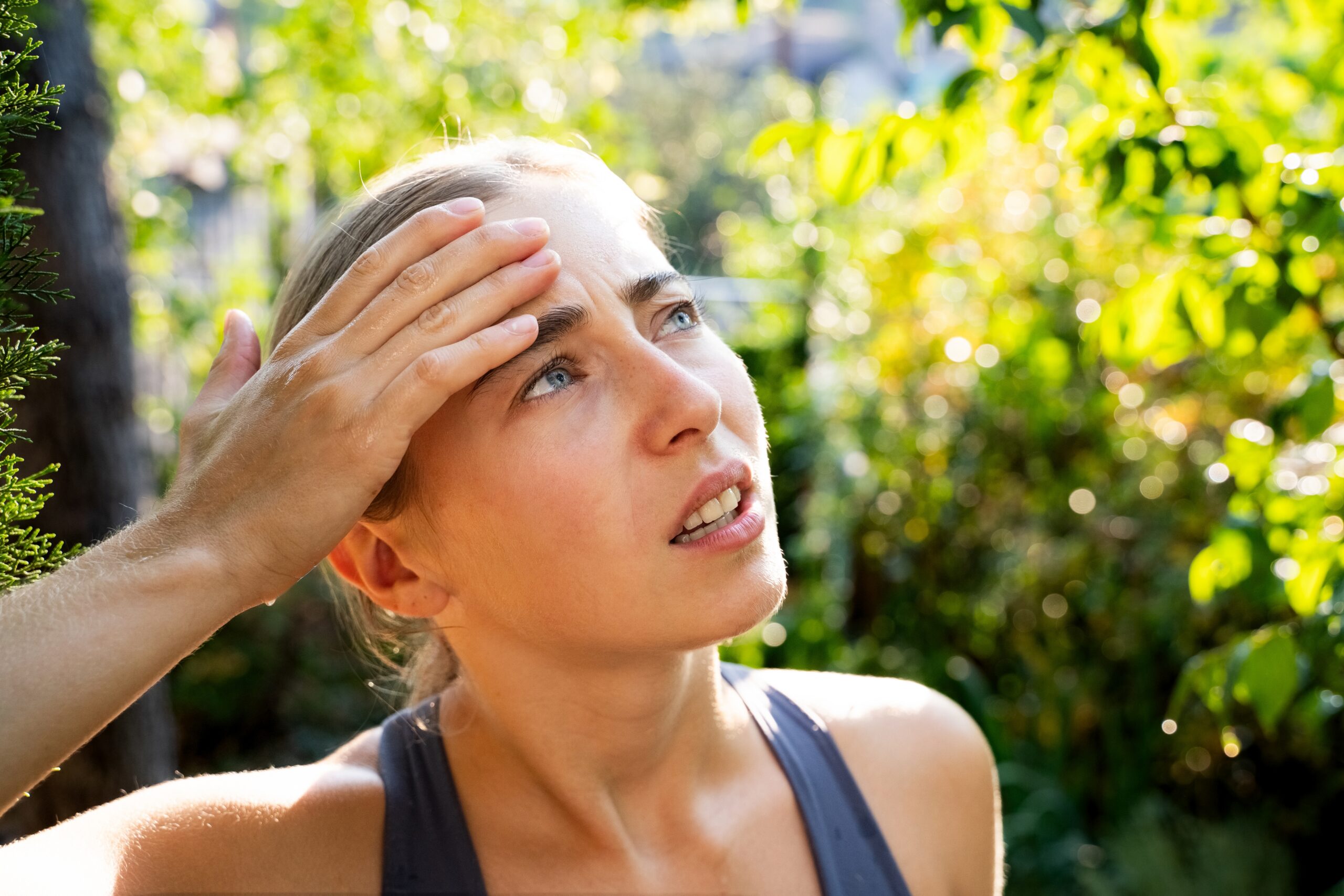 Woman wiping sweat from her forehead while standing outdoors in bright sunlight.