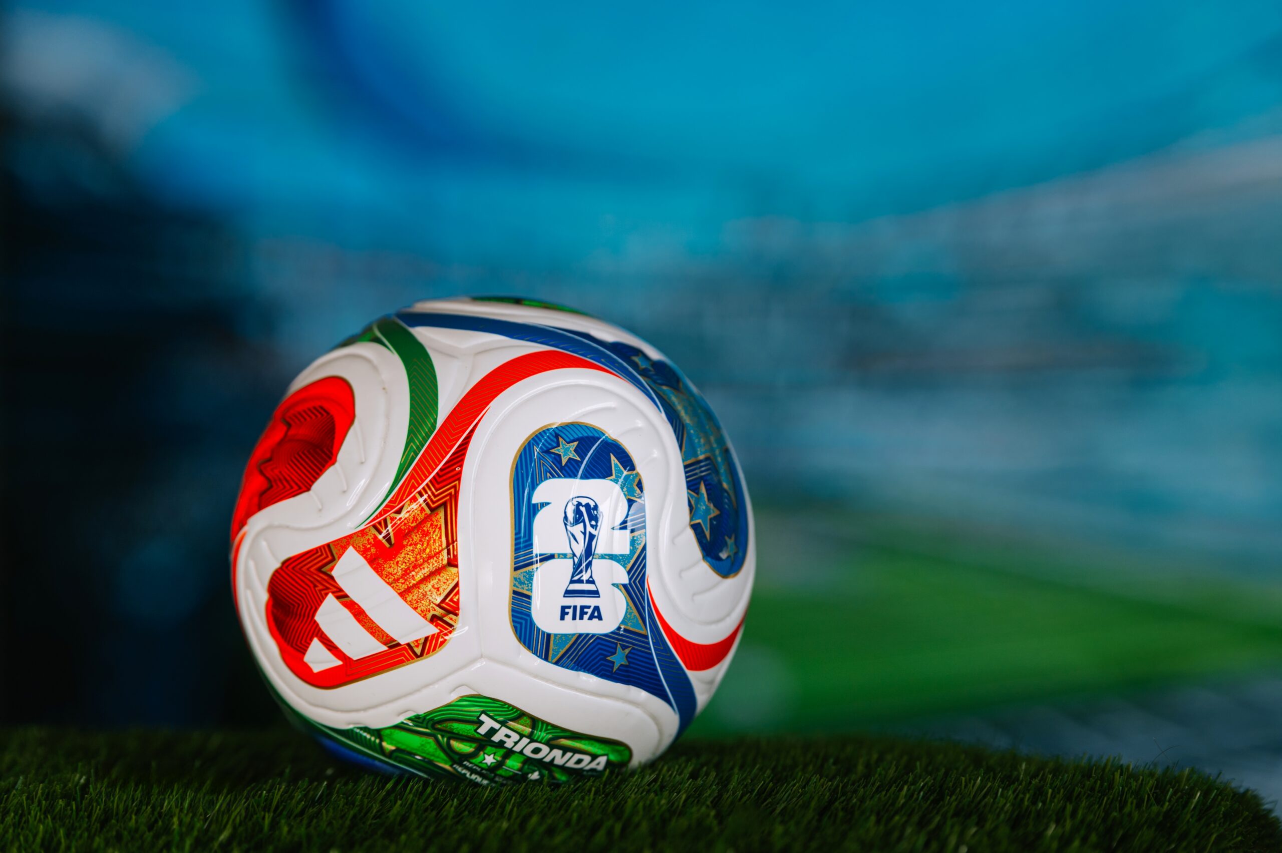 Official-style FIFA soccer ball resting on grass inside a stadium setting.