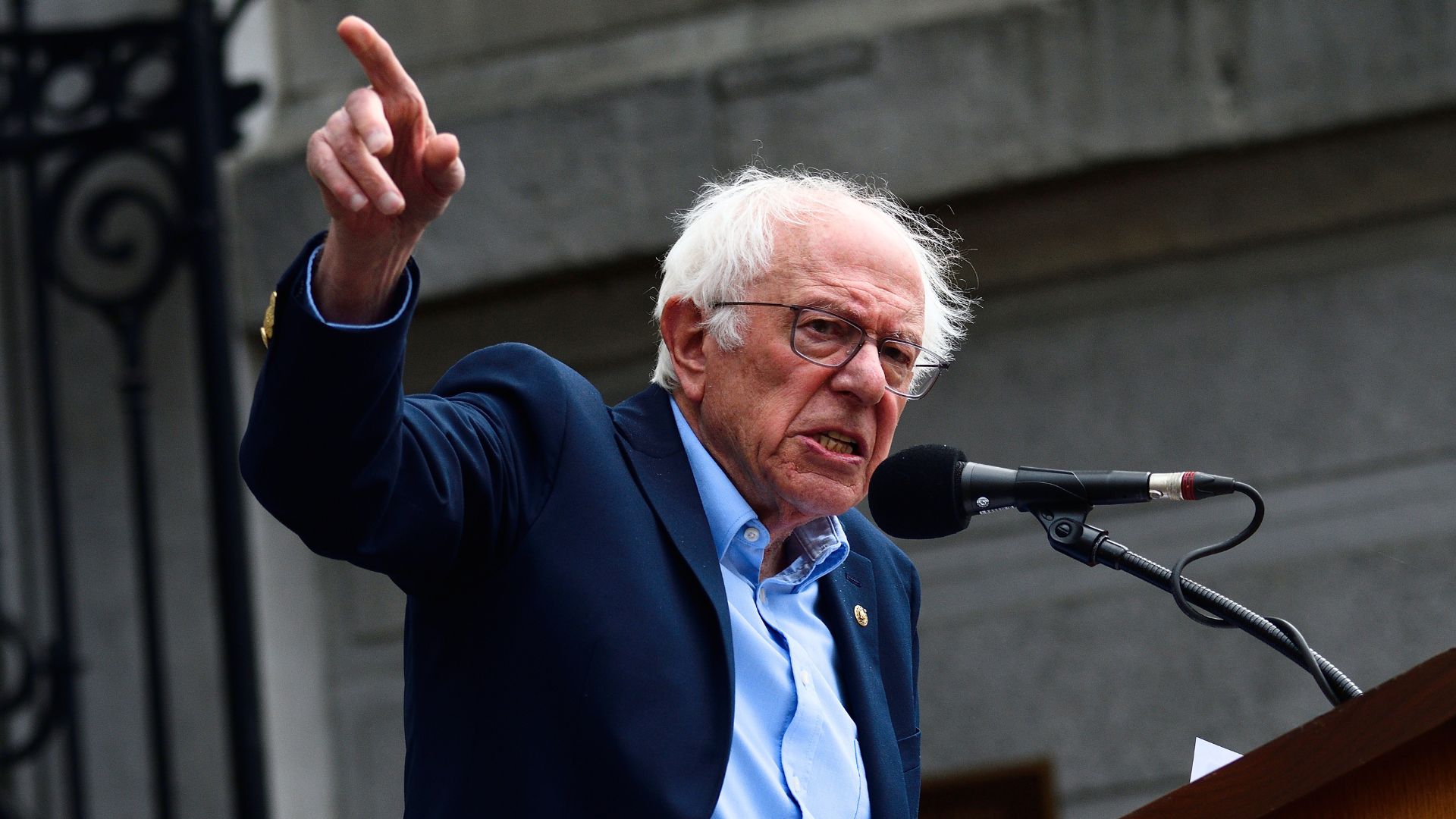 Bernie Sanders speaks at an outdoor rally while pointing into the crowd and addressing a microphone.