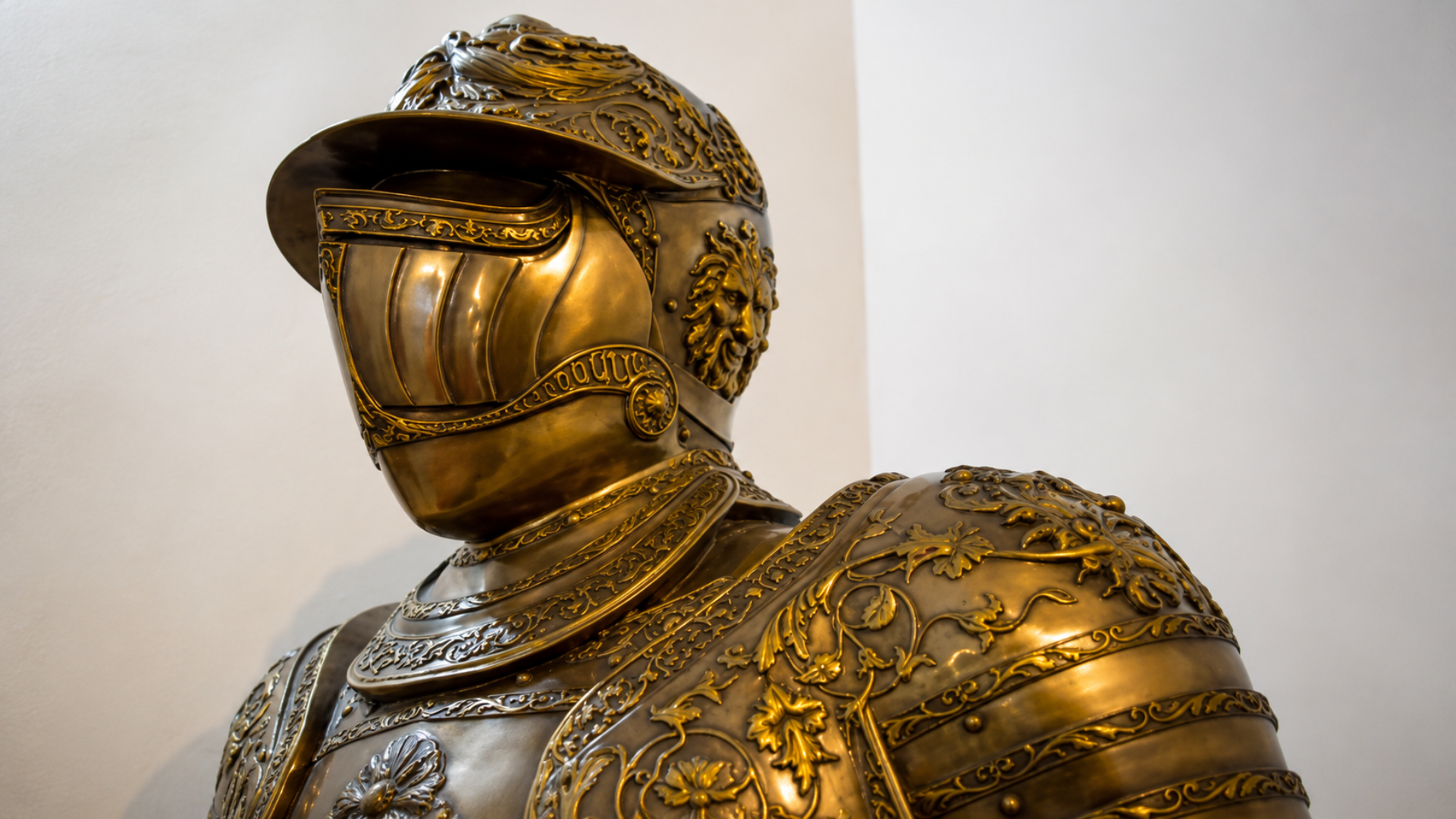 Ornate gold suit of armor displayed against a plain wall.