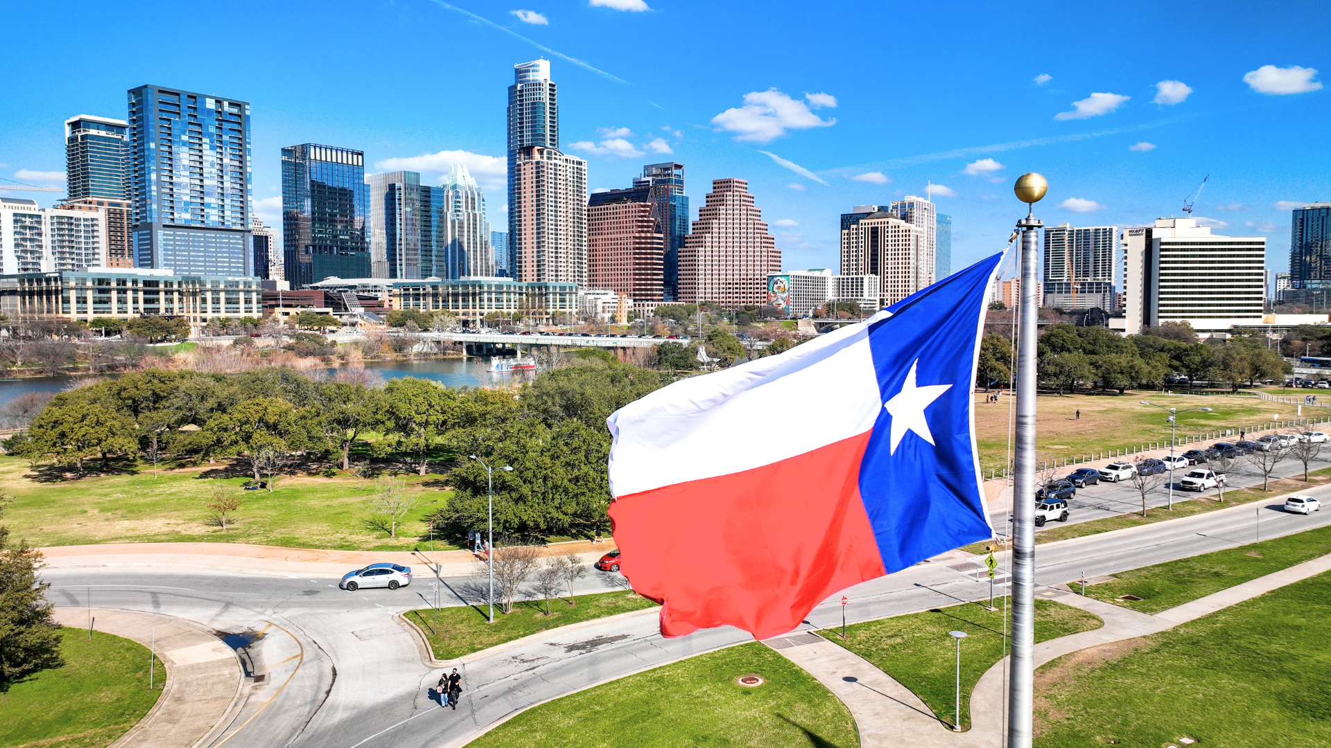 A large Texas state flag waving in the foreground against the downtown Austin skyline.