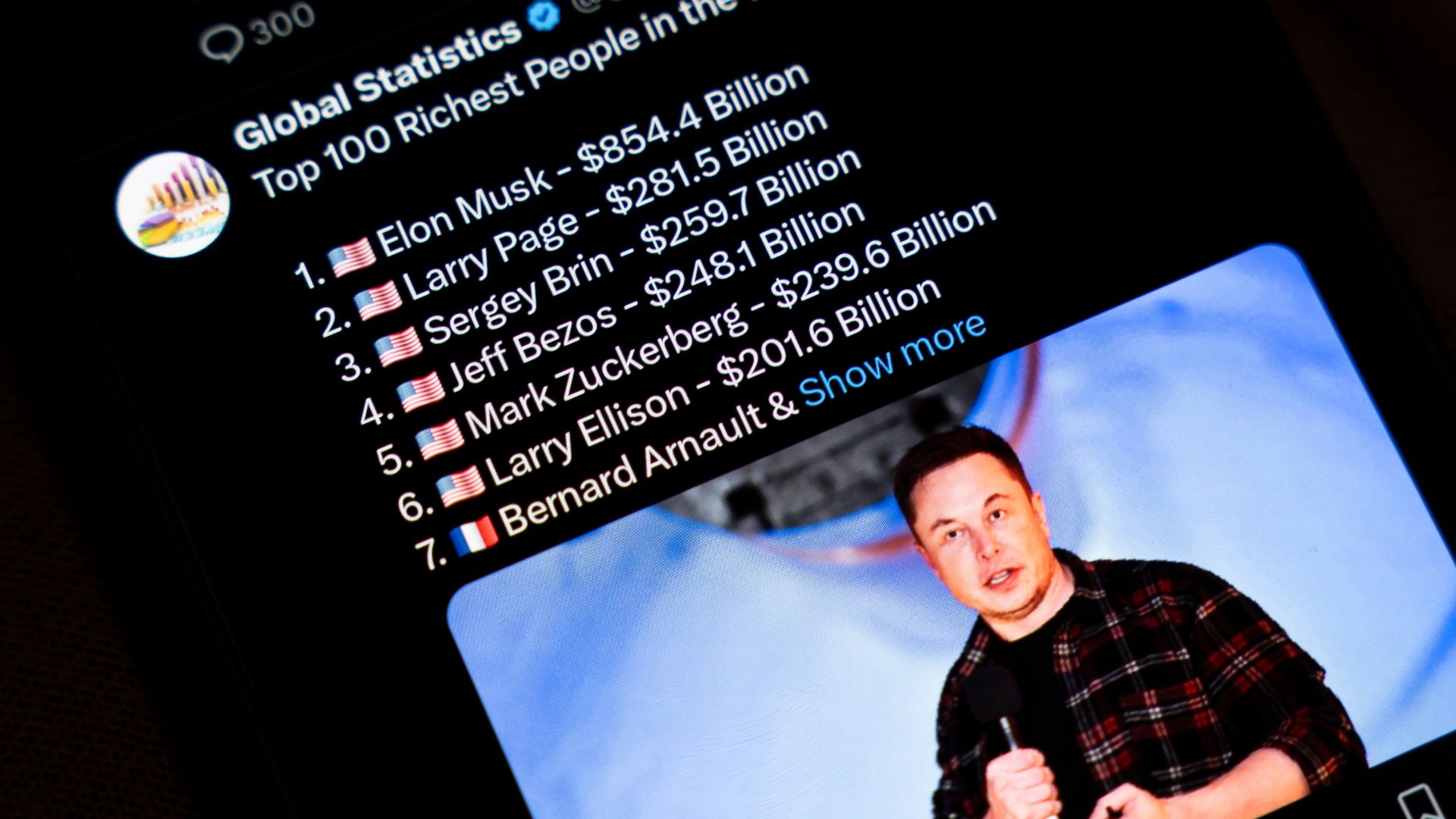 Smartphone screen displaying a social media post titled "Top 100 Richest People in the World" with Elon Musk listed first and other billionaires ranked below.