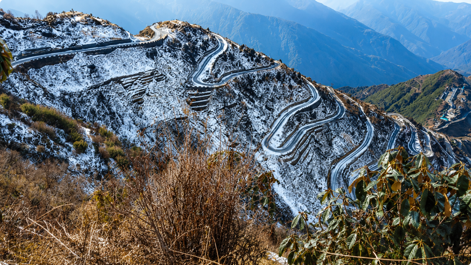 Winding mountain road cutting through snow-covered hills.