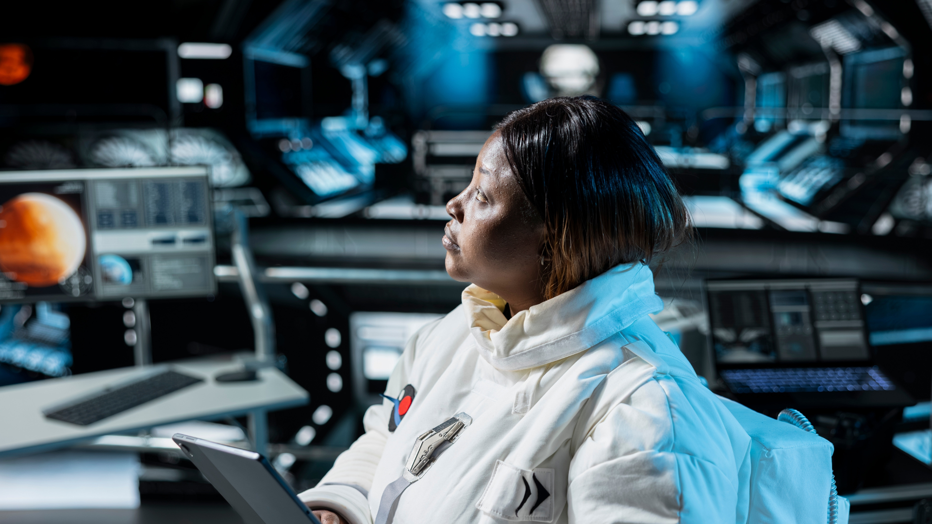 A female astronaut in a white spacesuit holding a tablet inside a futuristic spacecraft control room.