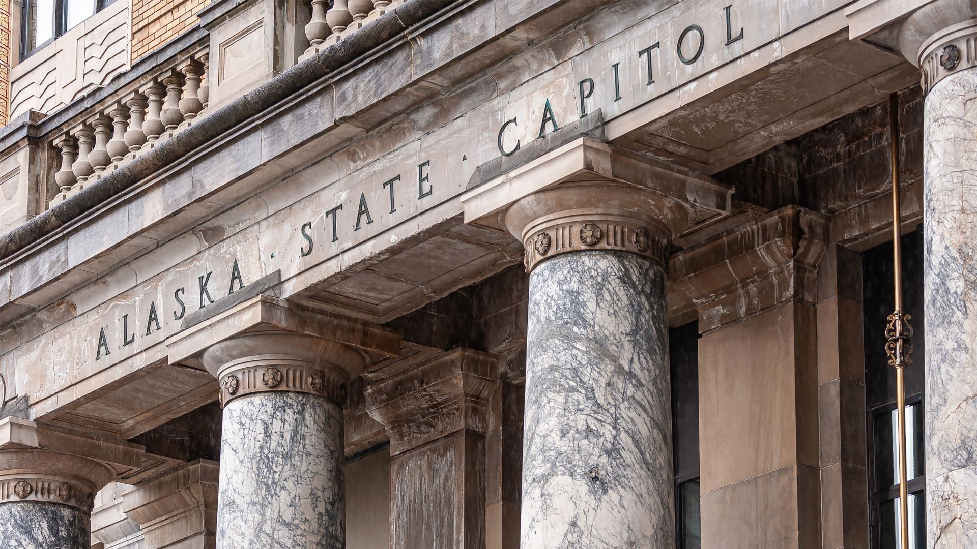Historic stone building with marble columns and the words "ALASKA STATE CAPITOL" engraved across the facade.